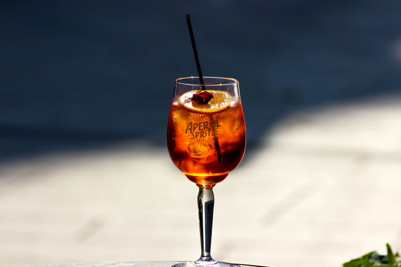 Close-up of a chilled Aperol Spritz with orange slice in sunny outdoor setting.